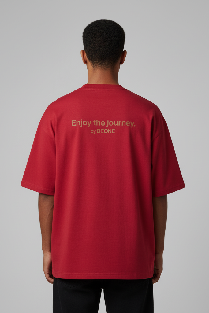 Person wearing a red t-shirt with 'Enjoy the journey. by BEONE' text on the back against a gray background